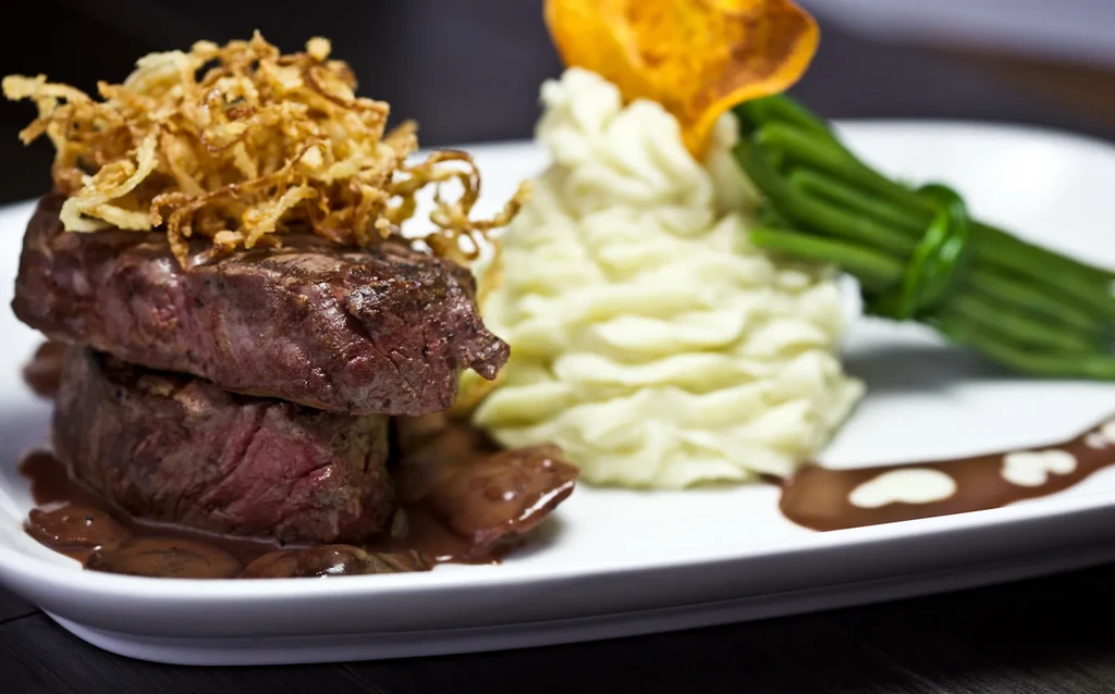 Steak topped with fried onions, mashed potatoes, and green beans.