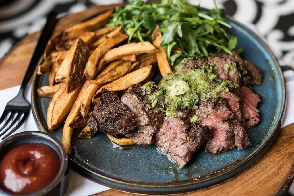 Steak, fries, and greens with a side of ketchup.