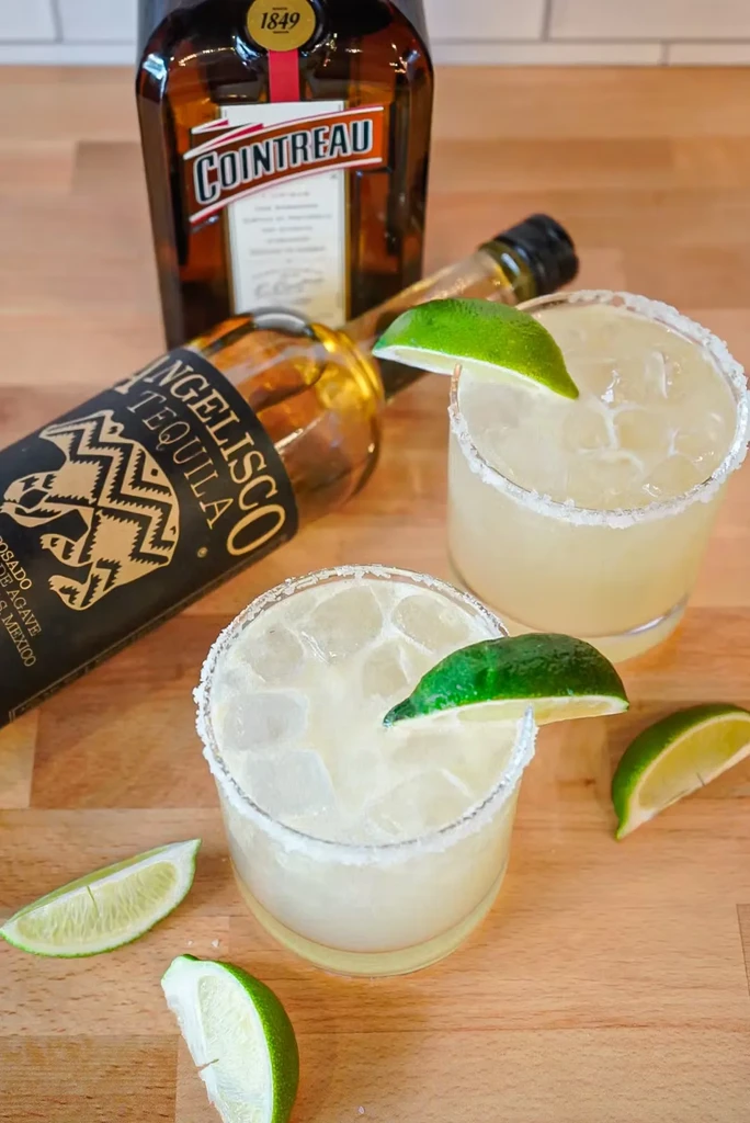 Two margaritas with lime and salt, tequila and Cointreau bottles.