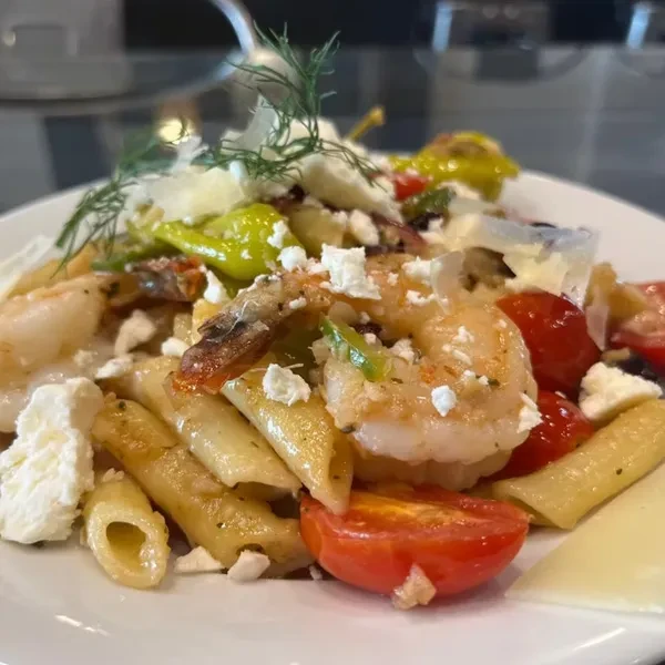 Penne pasta with shrimp, feta, peppers, and tomatoes on a white plate.