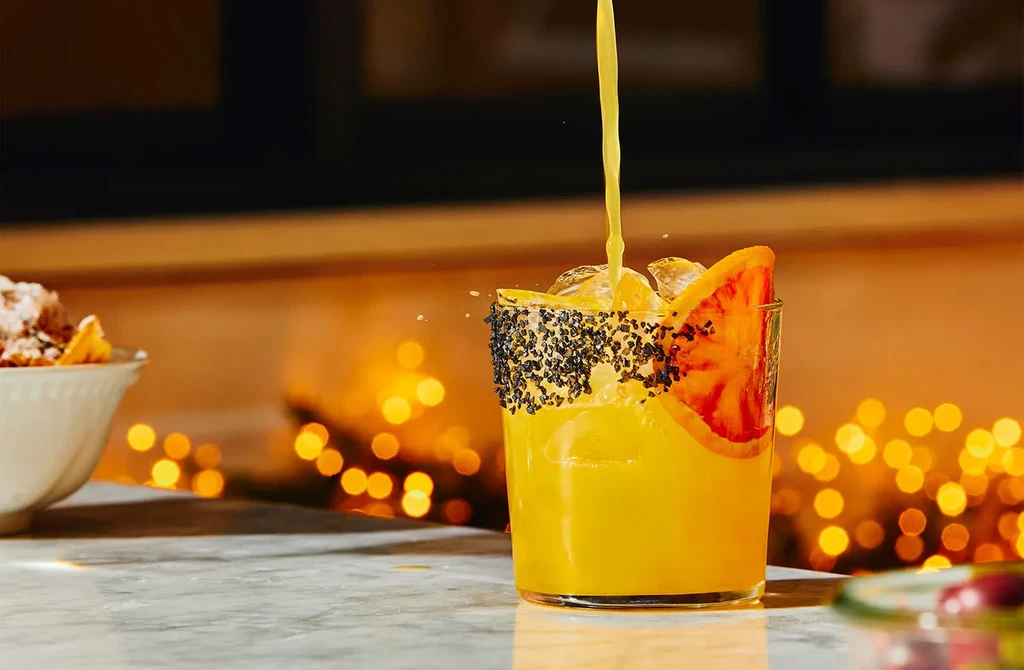 Orange juice pouring into a glass with a citrus garnish.