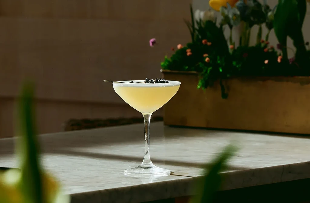 Light yellow cocktail in a martini glass garnished with lavender sprigs.