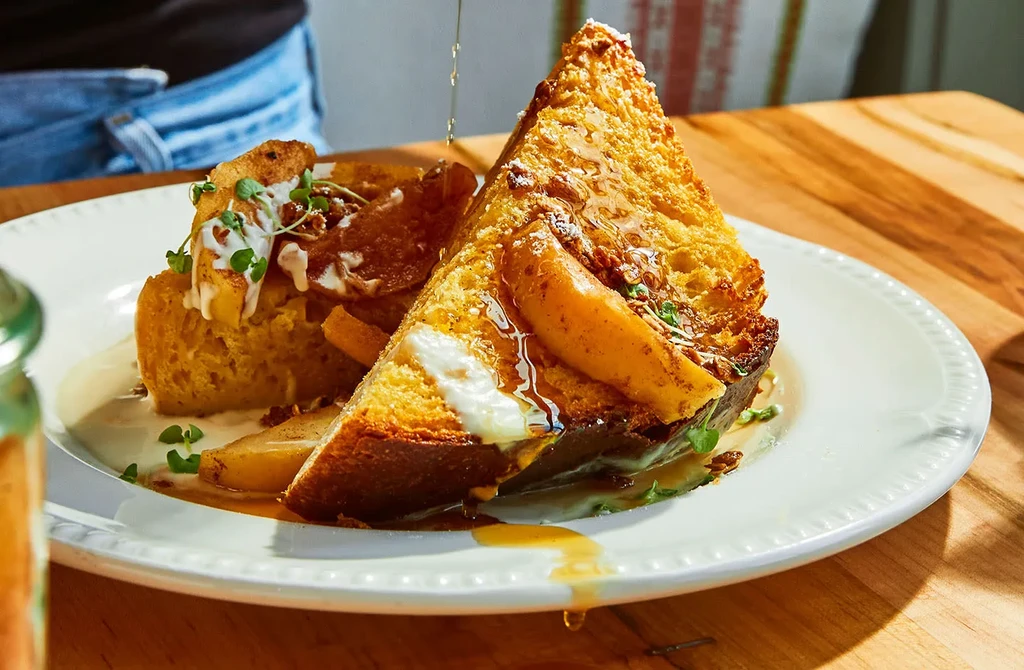Maple syrup pouring over French toast with pears and cream.