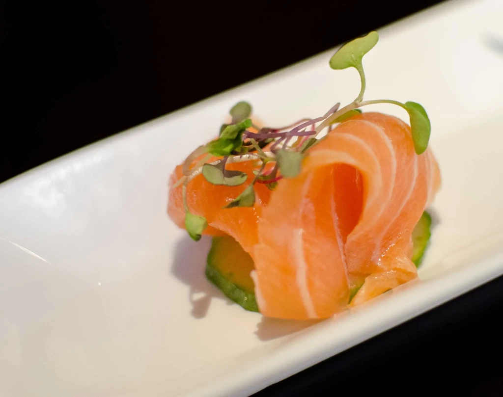 Orange salmon rolls topped with microgreens on a white plate.