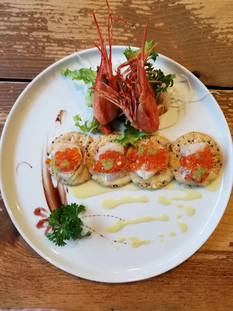 A white plate with shrimp heads, crackers with fish roe, and sauce.