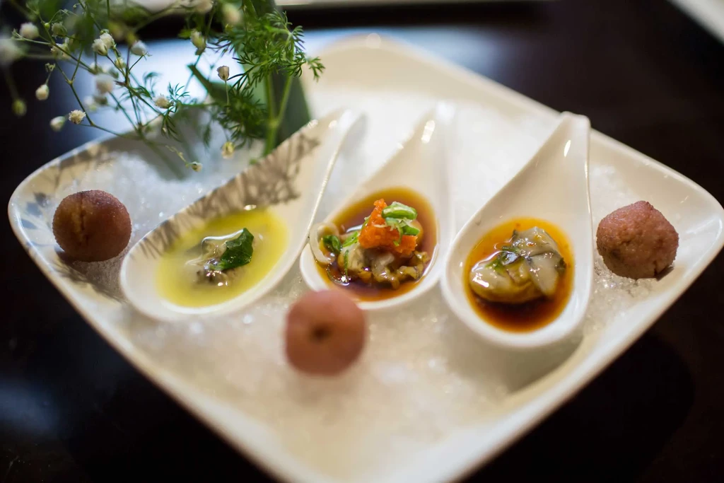 Three spoons of appetizers with oysters on a bed of ice.