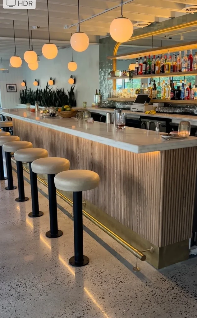 Modern bar with globe lights, ribbed wood, and white stools.