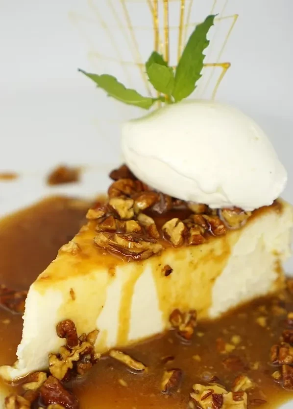 Cheesecake slice with walnuts, caramel sauce, ice cream, and mint.