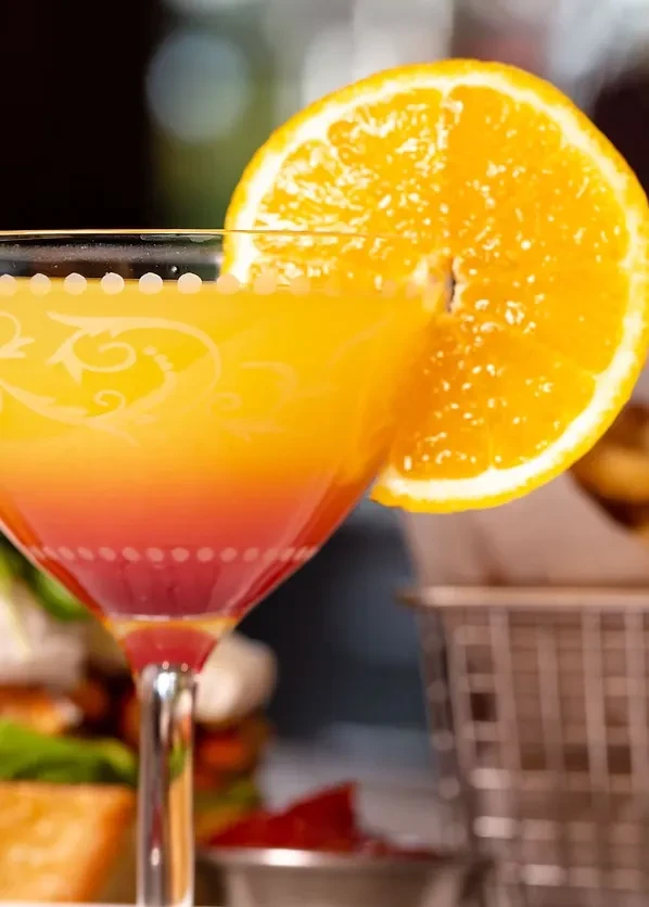 Close-up of a gradient orange drink in an etched martini glass with an orange slice.