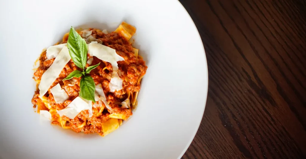 Pasta with bolognese sauce, parmesan, and basil on a white plate.
