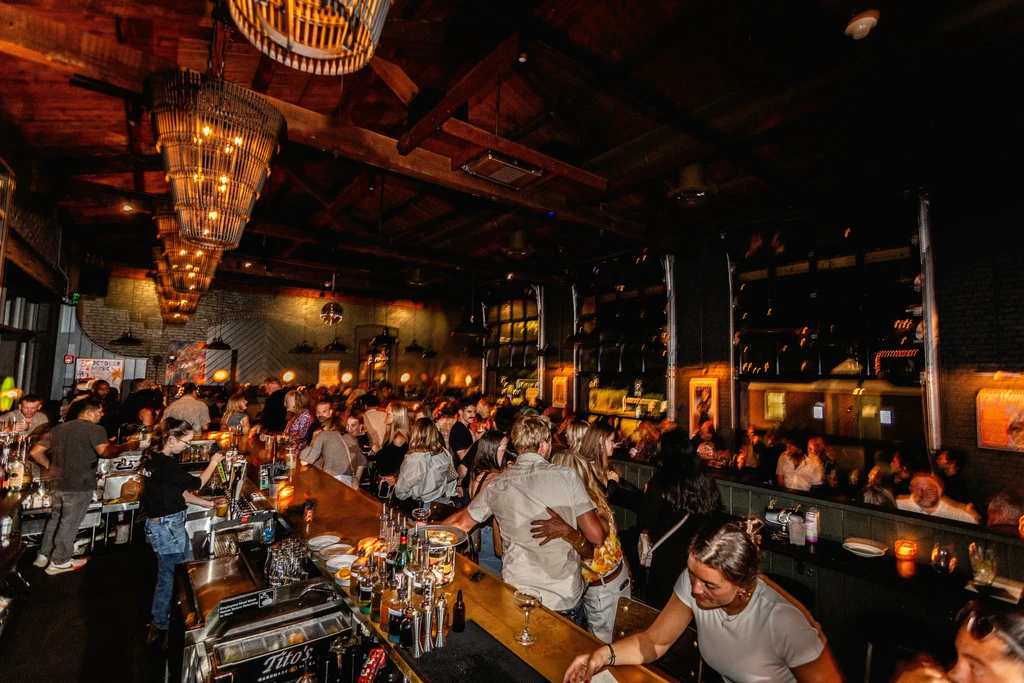 A bustling, dimly lit rustic bar with many socializing patrons.