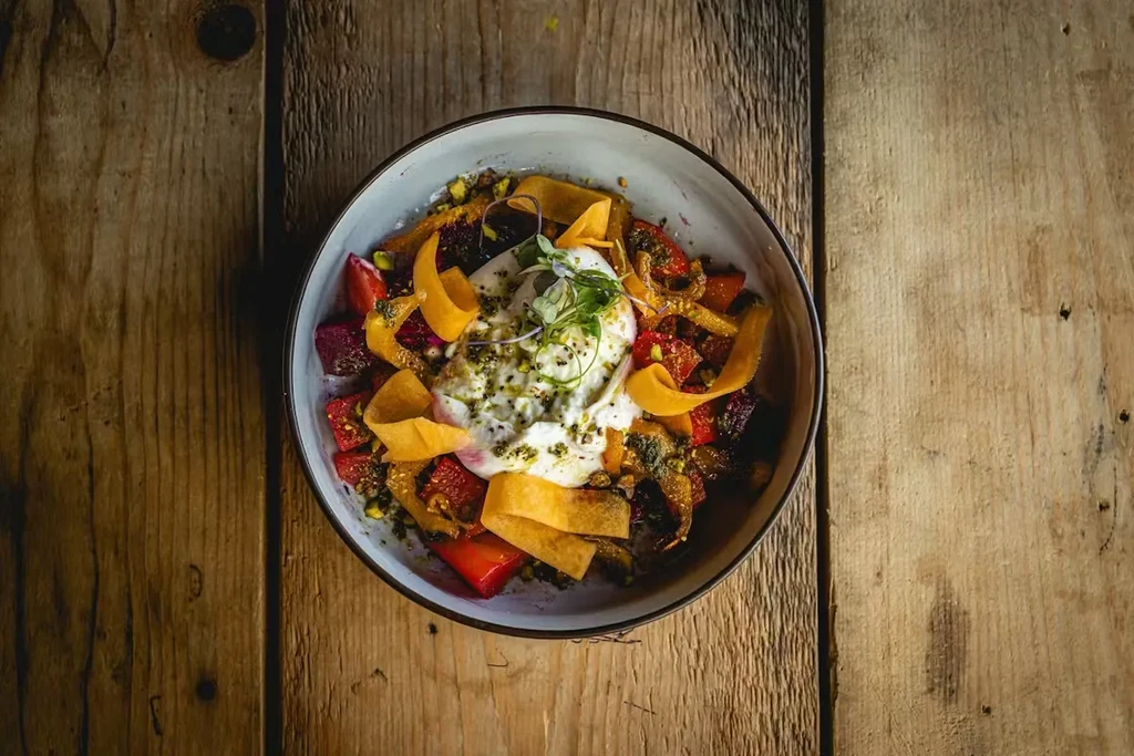 Colorful salad bowl with creamy burrata cheese on a rustic table.