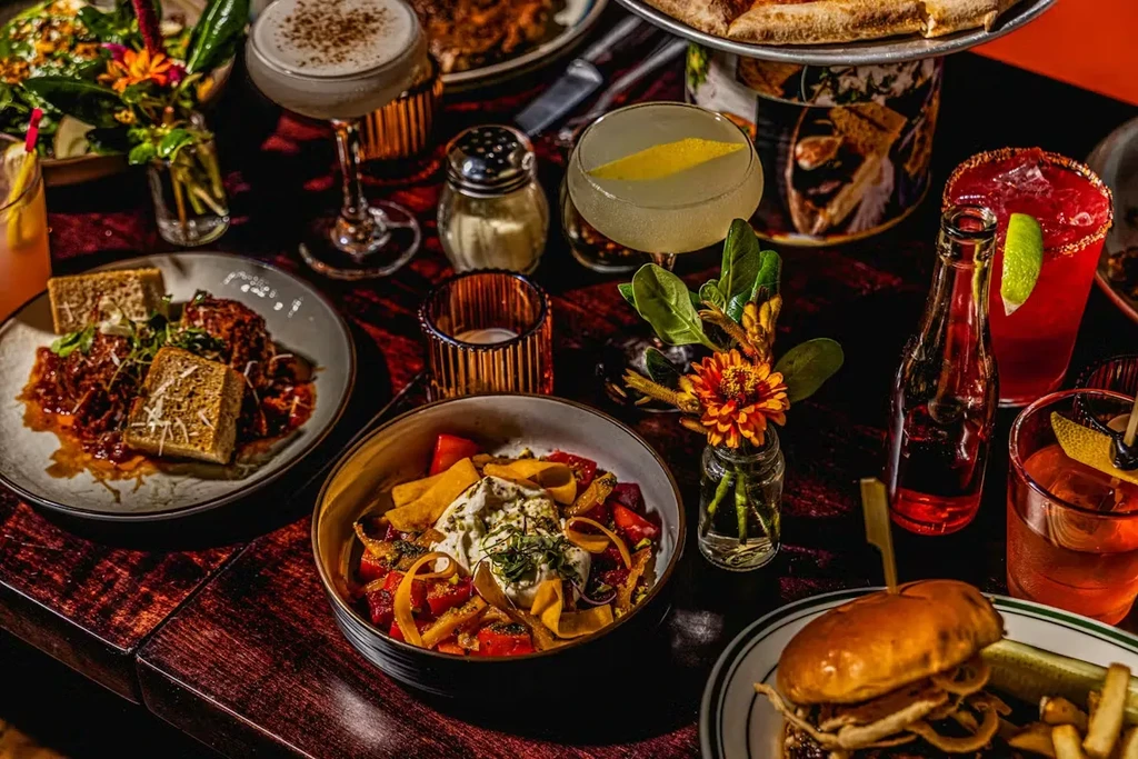 A dining table laden with various food dishes, cocktails, and flowers.