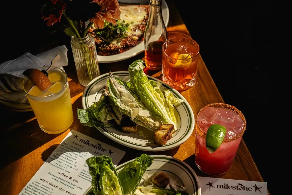 Restaurant table with Caesar salads, three cocktails, baked dish, and menus.