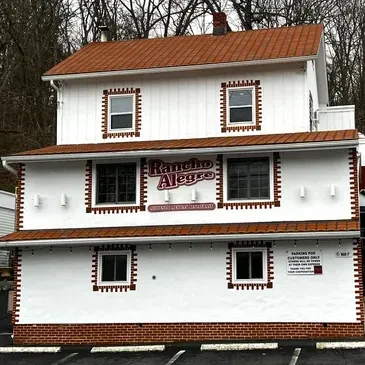 White two-story "Rancho Alegre" restaurant building with reddish-brown roof and brick.