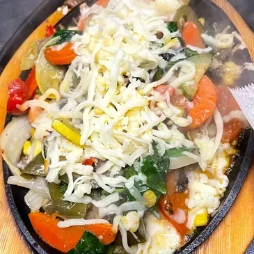 Vibrant, sizzling vegetables with melted cheese in a cast-iron skillet.