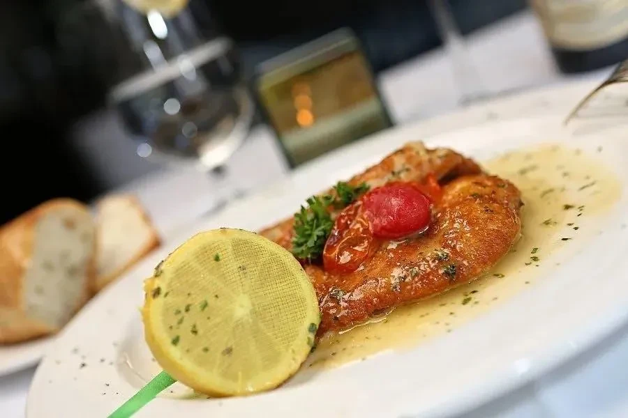 Pan-seared fish with tomato and lemon slice on a white plate.