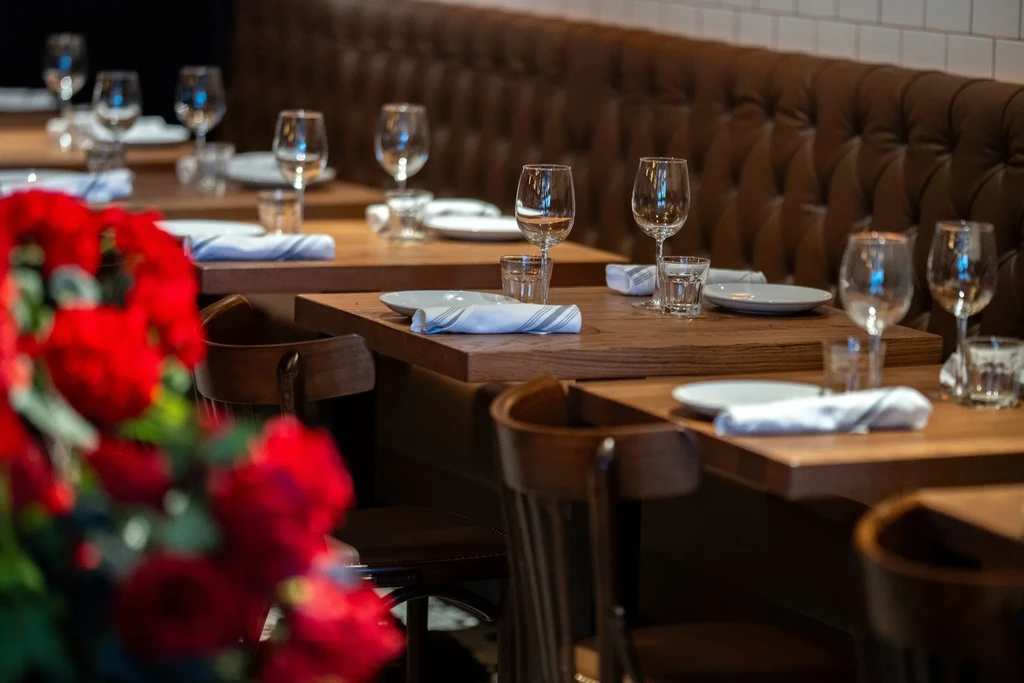 Empty restaurant with wooden tables, brown leather booths, and red flowers.