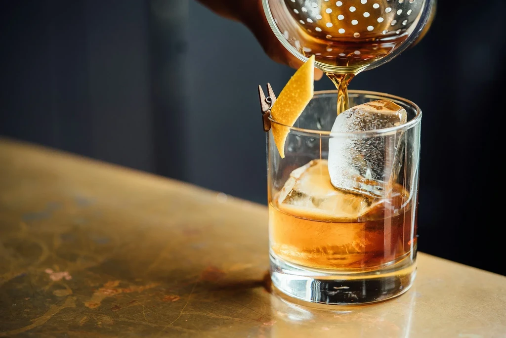 Amber liquid being poured into a glass with large ice cubes.