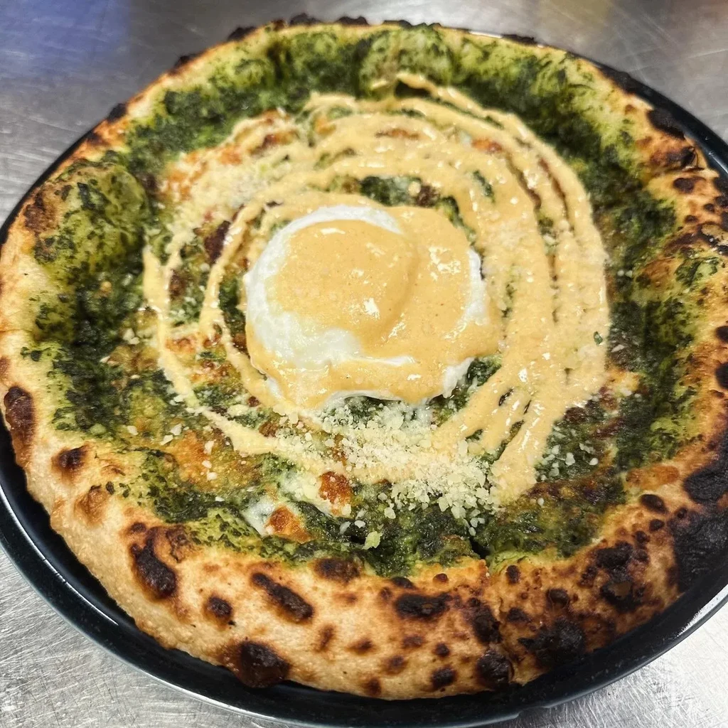 Pizza with green pesto, egg, and sauce on a dark plate.