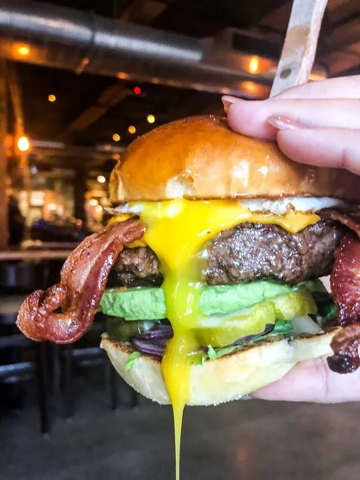 A hand holding a burger with a runny fried egg and bacon.