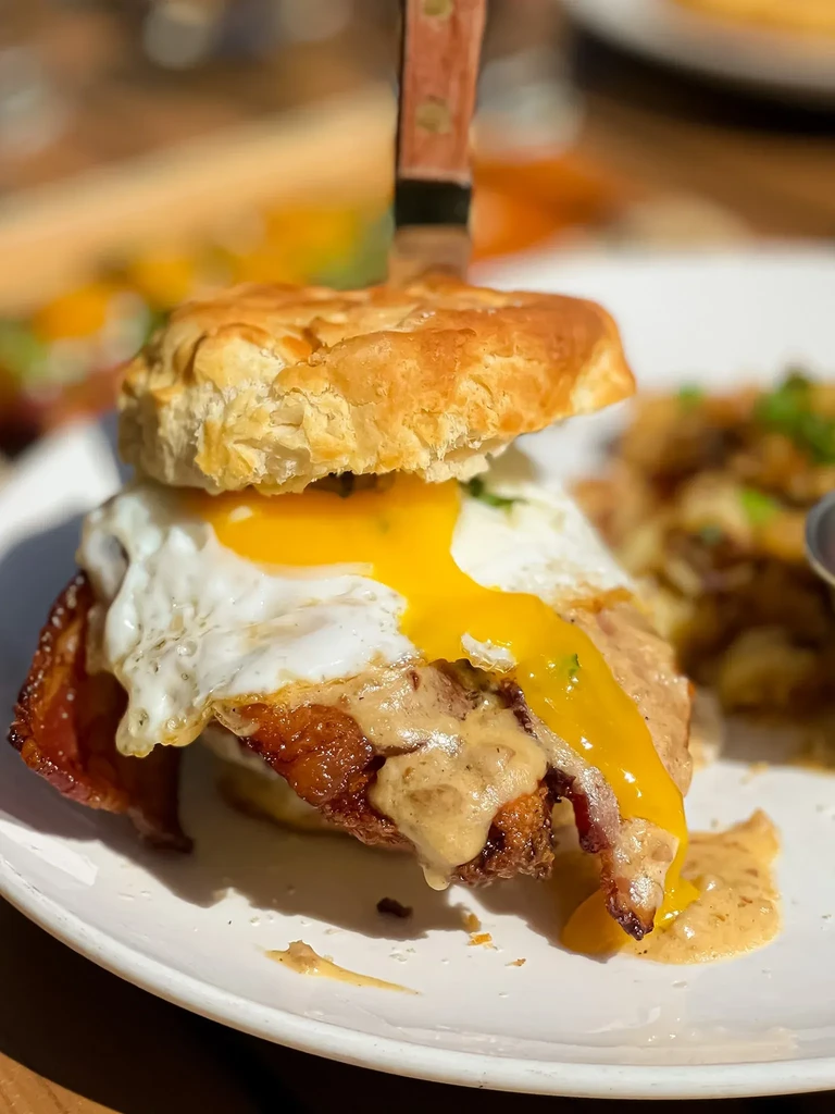 A tall biscuit sandwich with fried egg, bacon, gravy, and a knife.