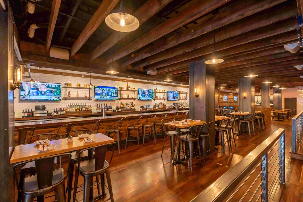 Spacious bar and restaurant with high ceilings, exposed beams, and a long bar.