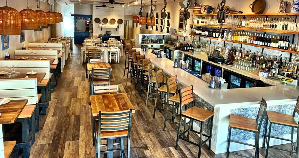 Empty restaurant with a long bar and many wooden tables and chairs.