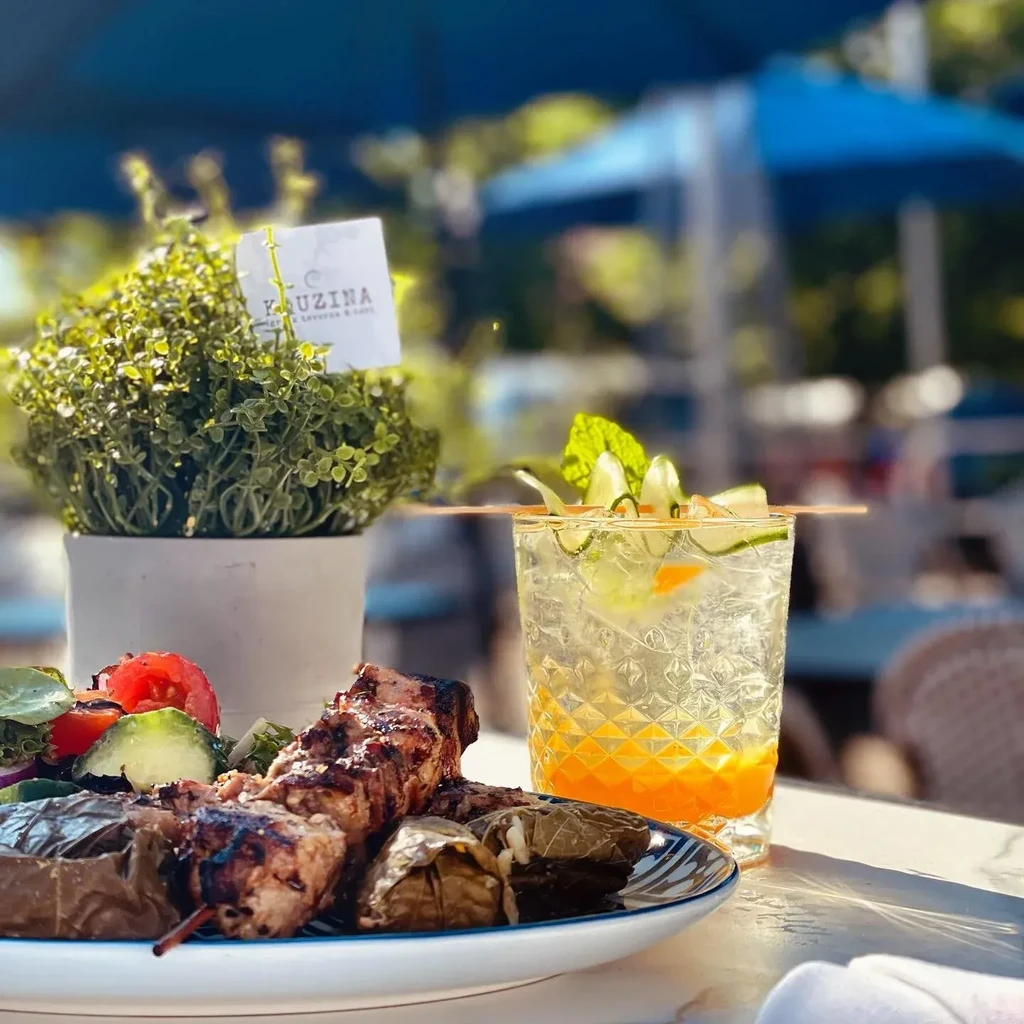 Grilled souvlaki and dolmades with a drink on an outdoor table.