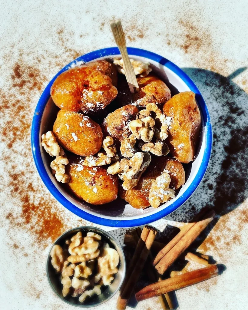 A bowl of fried dough, walnuts, and cinnamon sticks on a table.