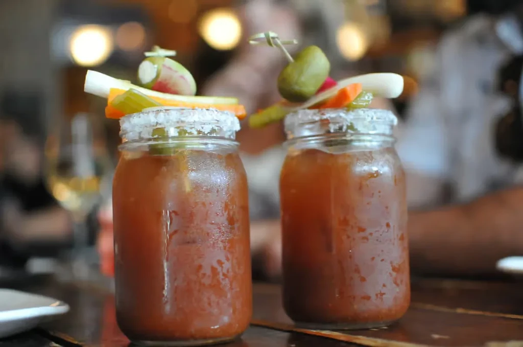 Two bloody mary cocktails in mason jars garnished with celery and pickles.