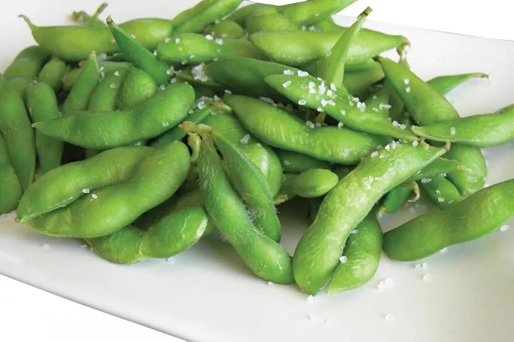 A close-up of bright green edamame pods sprinkled with coarse salt.