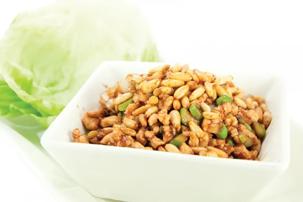 White bowl of chicken and pine nut lettuce wraps, with lettuce in background.