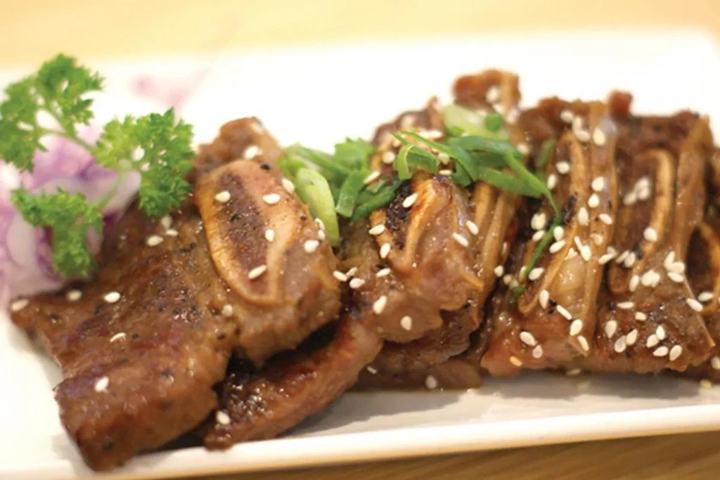 Short ribs with sesame seeds, green onions, and parsley on a white plate.