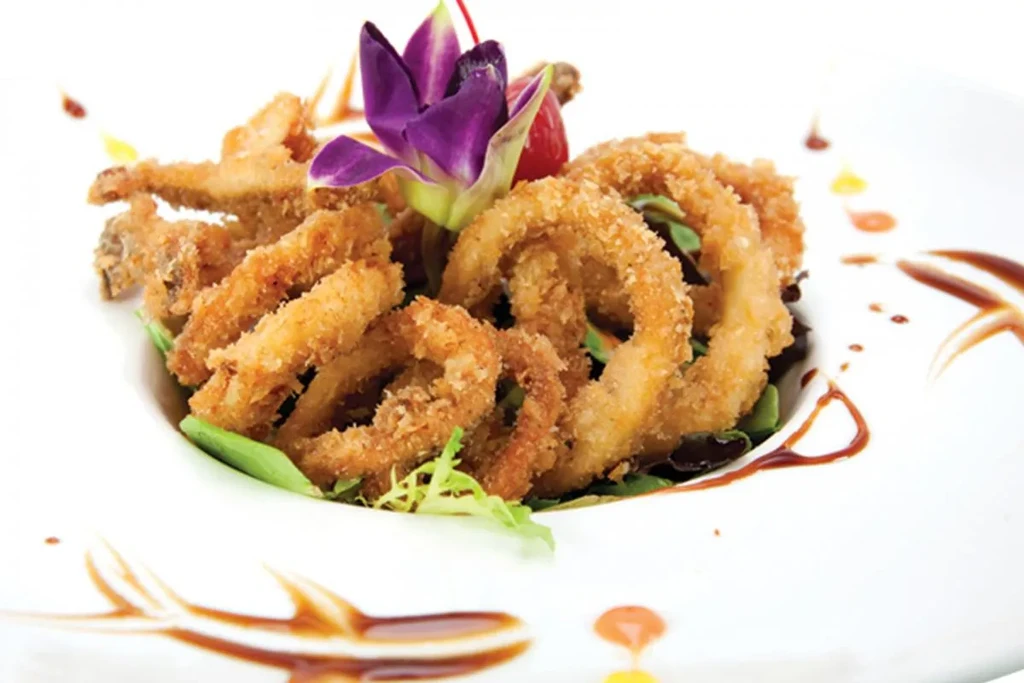 Fried calamari rings and strips with a purple flower garnish on a white plate.