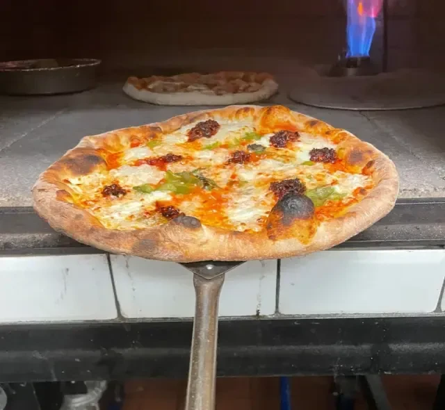 A pizza is removed from an oven on a metal peel.