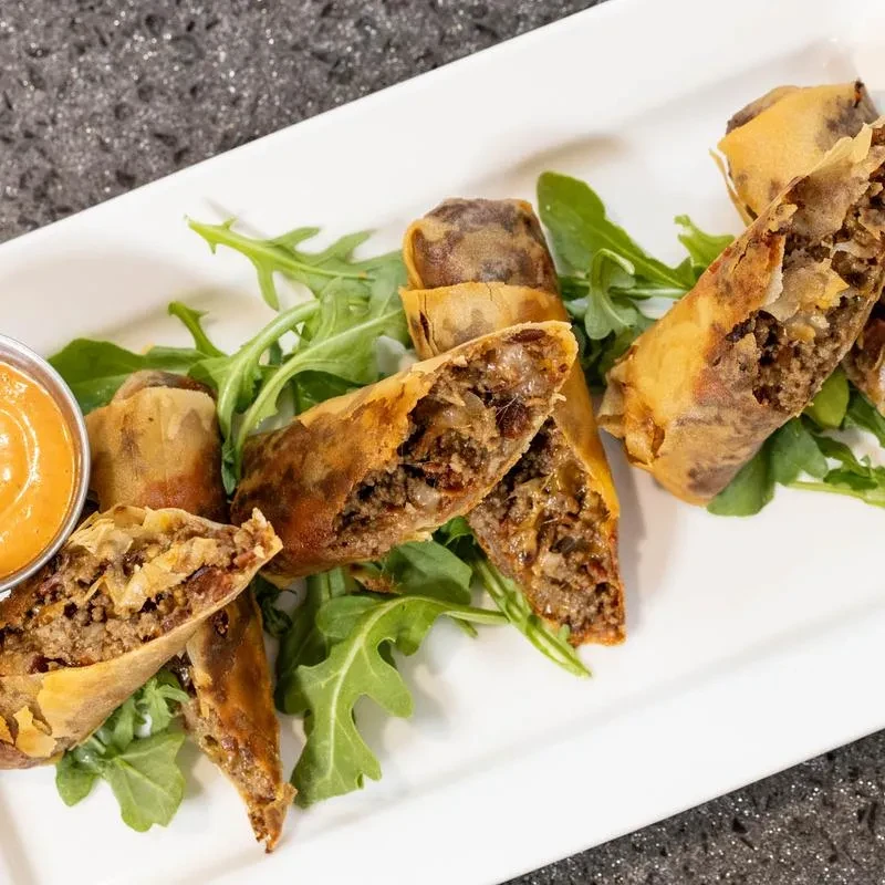 Several cut egg rolls with ground meat filling, greens, and sauce.