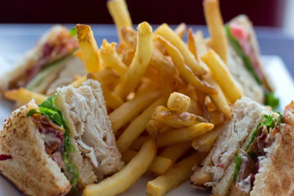 A plate of french fries surrounded by turkey club sandwiches.