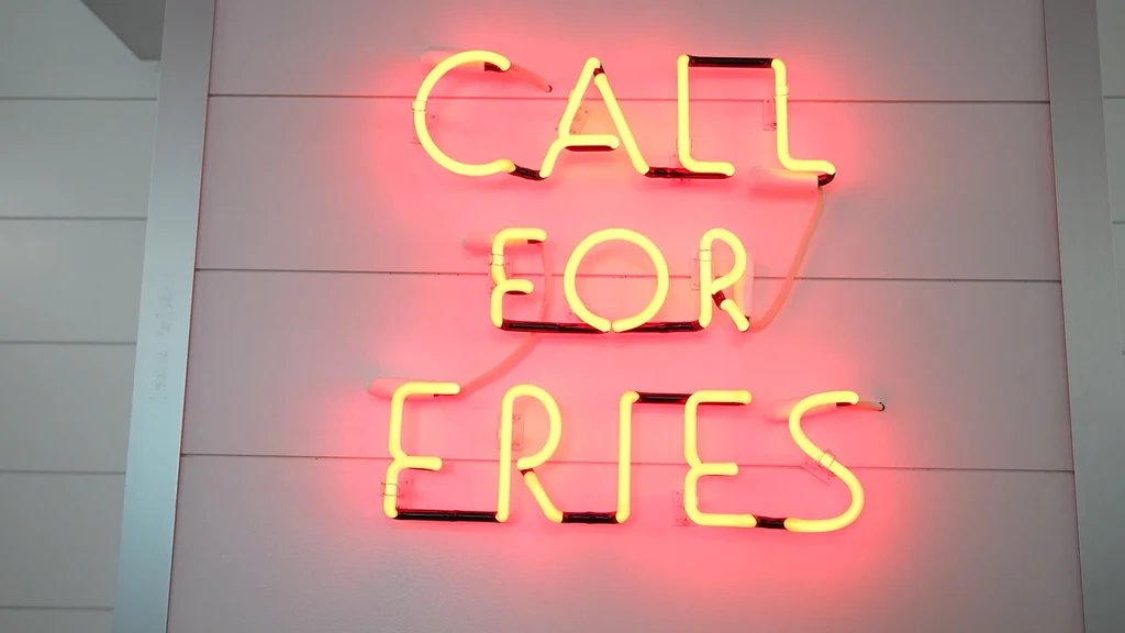 Yellow neon sign reading "CALL FOR FRIES" on a pink wall.
