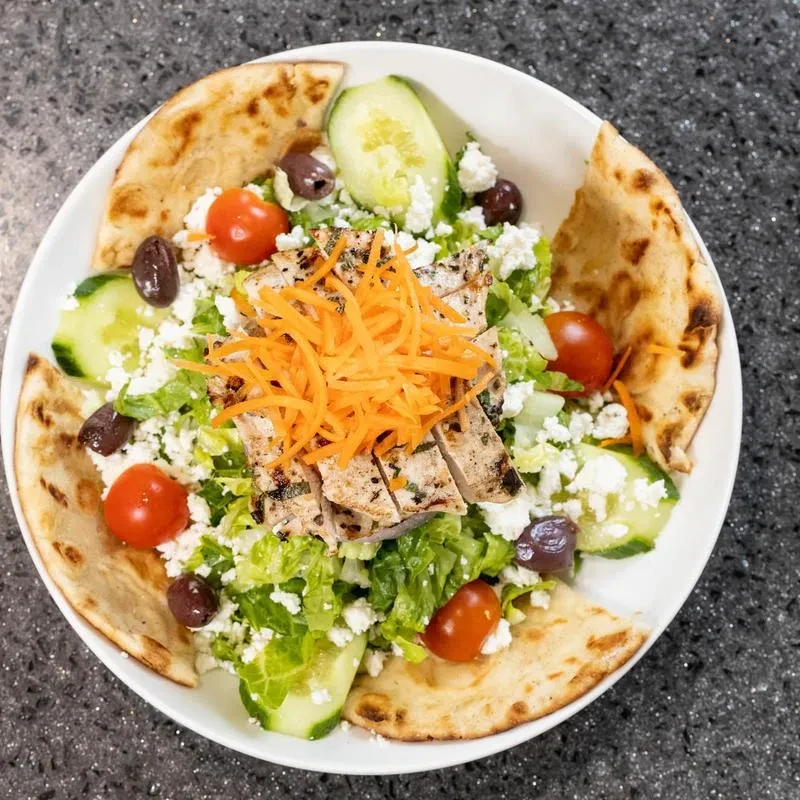 Overhead shot of a Greek salad with grilled chicken and pita bread.