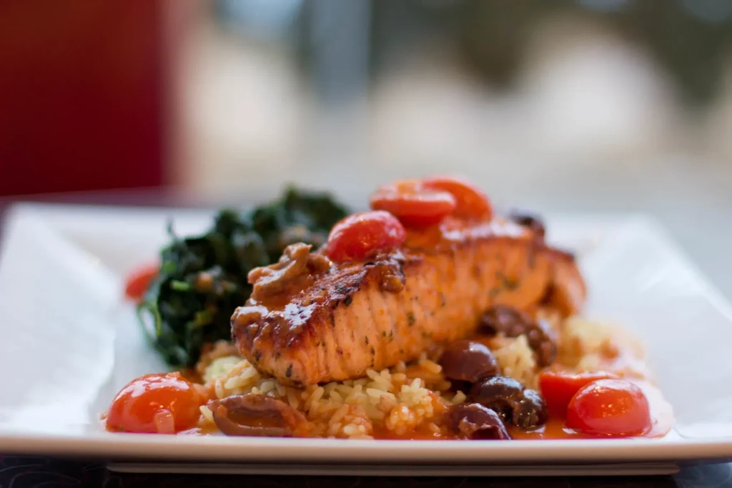 Close-up of a salmon filet with rice, spinach, tomatoes, and olives.
