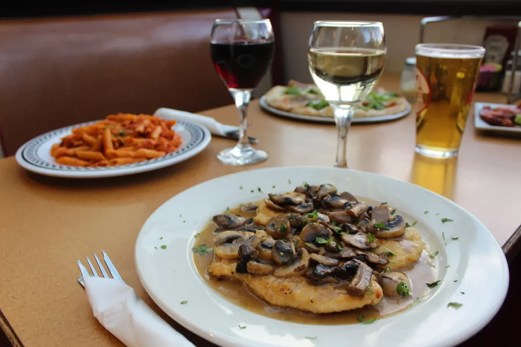 Plates of Italian food, wine, and beer on a restaurant table.