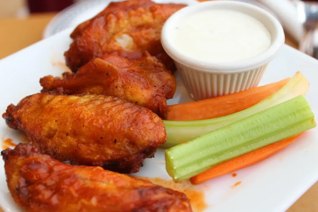 Plate of buffalo wings, blue cheese dressing, carrots, and celery sticks.
