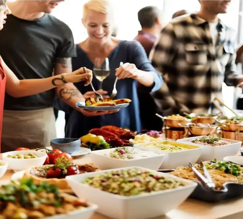 People serve themselves at a buffet with numerous dishes and a drink.