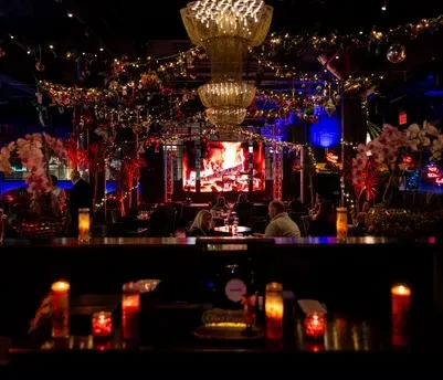 A restaurant or club at night, with patrons, chandeliers, and screens.