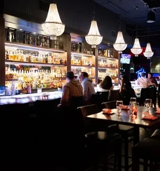 People at a bar with crystal chandeliers and a well-stocked liquor shelf.