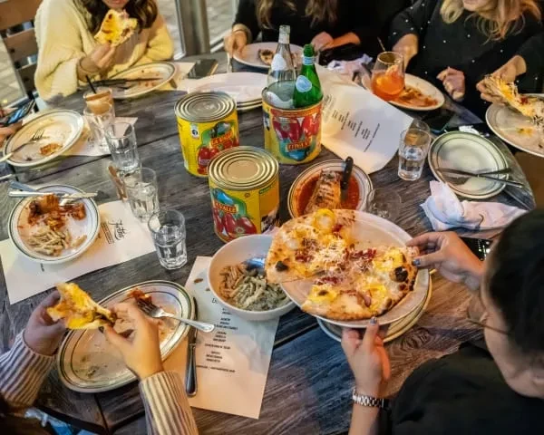 Friends enjoying pizza and pasta dishes at a restaurant table.