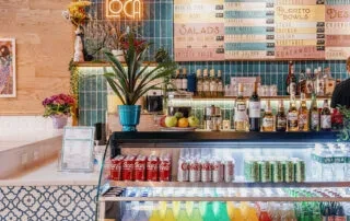 A cafe counter with bottles, drinks, and a menu board overhead.