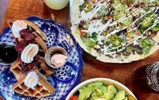 Waffles with berries and whipped cream next to a large flatbread pizza.