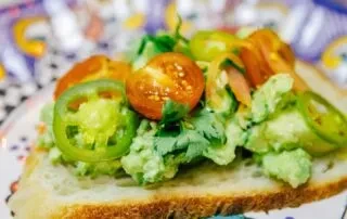 Slice of bread topped with avocado, halved tomatoes, and sliced peppers.